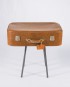 Mesa vintage compuesta por cuatro patas metálicas y una antigua maleta de piel color camel